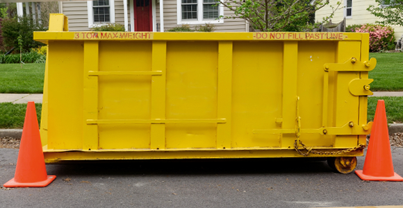 Yellow dumpster placed in street with traffic cones