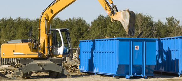 excavator dumping debris into a 30 yard dumpster