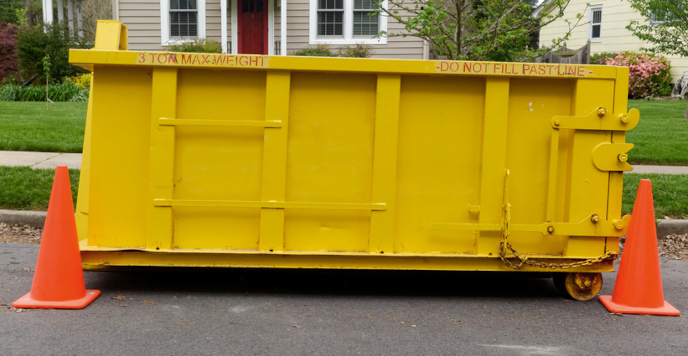 Yellow dumpster on street with orange cones for safety