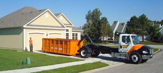 truck dropping off dumpster in driveway of home