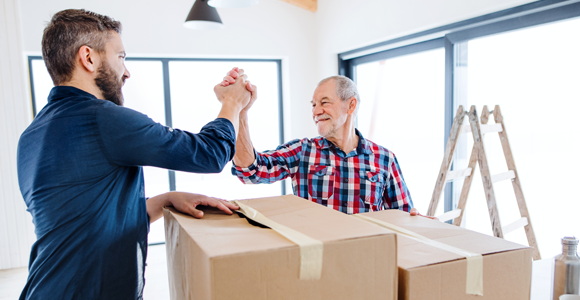 Elderly man and son high-fiving in room full of packing boxes