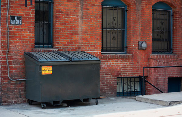 Commercial dumpster outside against brick building