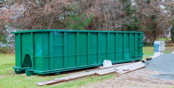 green dumpster and scrap wood sitting in yard