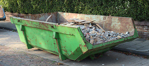 green dumpster in street with cement debris inside
