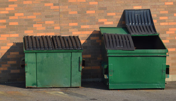 two commercial dumpsters side by side against brick building