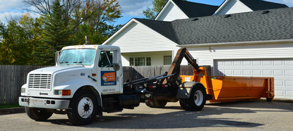 dumpster truck dropping off an orange dumpster in home's driveway