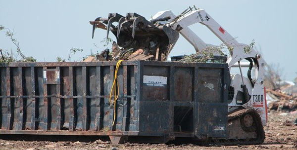 excavator dumping debris into a large dumpster