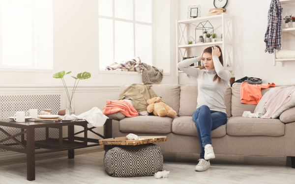 Stressed out woman sitting on couch covered in clutter