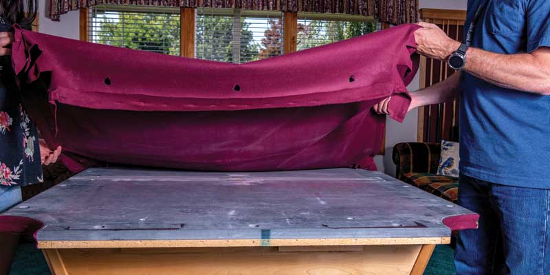 Two people removing felt from a pool table