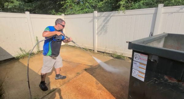 Commercial dumpster pad being cleaned with a pressure washer