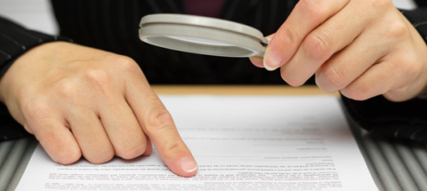 person closely inspecting a document with magnifying glass