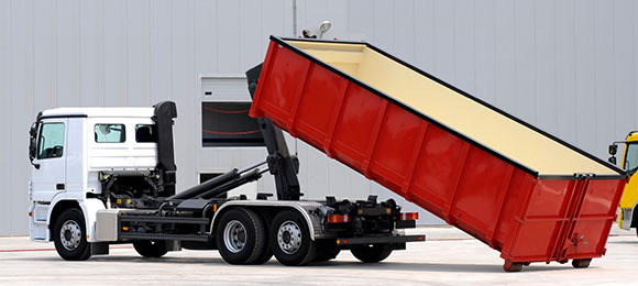 dumpster truck placing an empty red dumpster on the ground