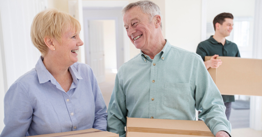 Happy senior couple moving boxes with professional help in the background