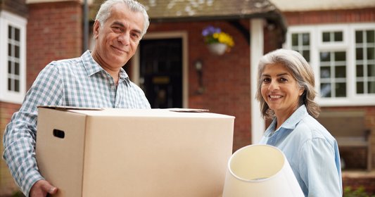 Happy senior couple with moving boxes in front of their new home