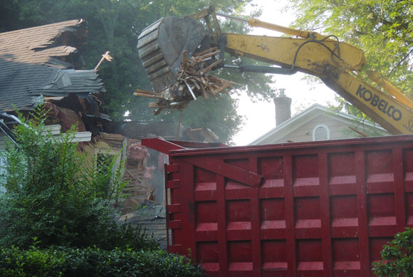 Excavator demolishing a house and putting debris into a 40 yard container