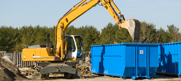 Excavator dumping debris into roll-off dumpster