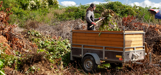 Man putting yard waste into a small trailer dumpster