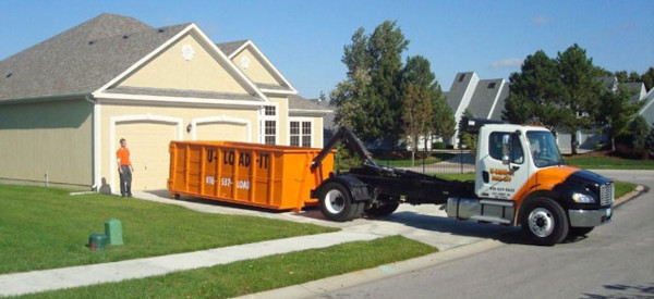 dumpster truck dropping off dumpster at house