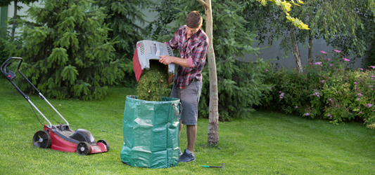 man dumping grass clippings from lawn mower into a trash bin