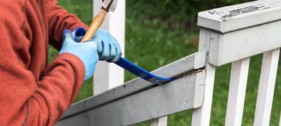 person prying up deck railing with crow bar