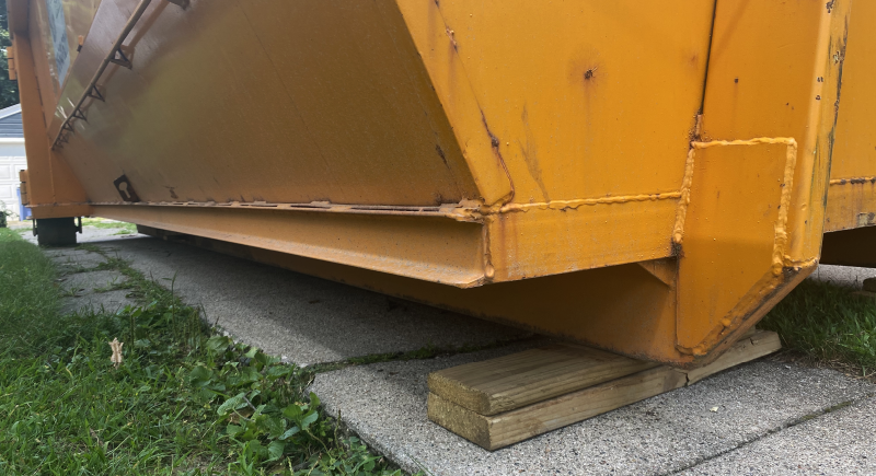 planks placed under dumpster on driveway