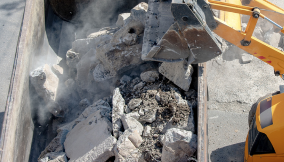 excavator dumping concrete debris in dumpster