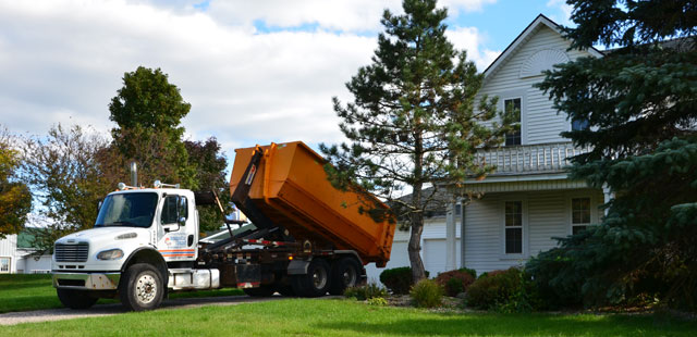 dumpster truck dropping off a dumpster on a driveway