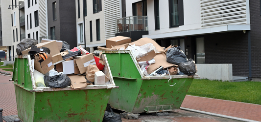Two roll-off dumpsters full of household junk in front of apartment building