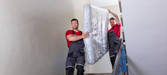 Junk removal crew carrying mattress down flight of stairs