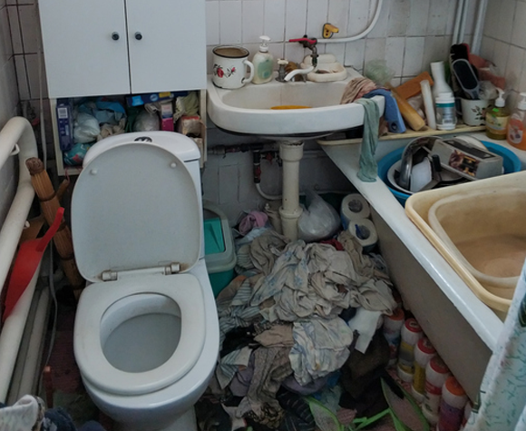 dirty bathroom covered in with piles of clothes and junk