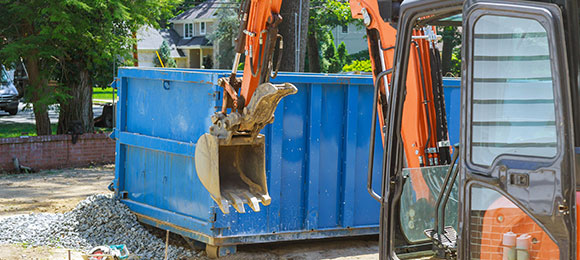 excavator loading concrete debris into dumpster