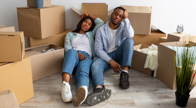 Exhausted couple sitting on the floor in a room full of moving boxes