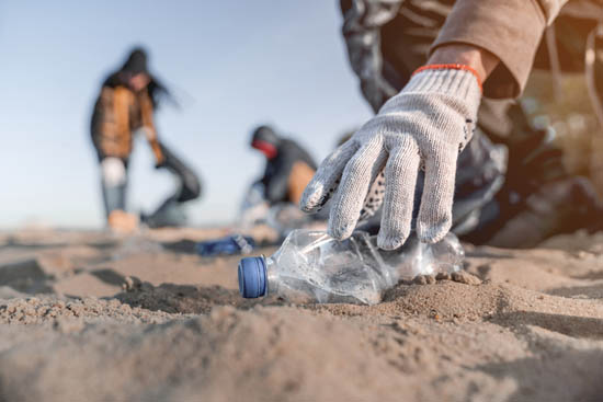 person picking up littered plastic bottle on beach