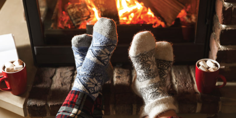 feet with cozy socks kicked up in front of fireplace with hot cocoa